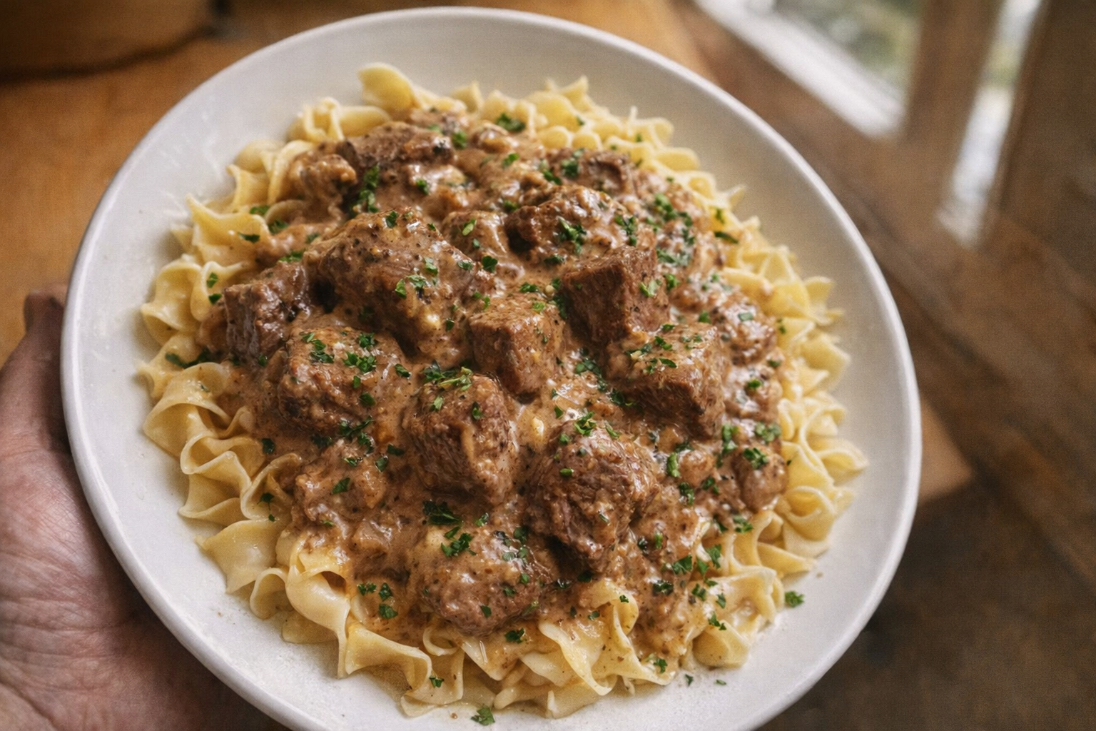 A top-down shot of beef stroganoff served over egg noodles, garnished with fresh parsley, creamy sauce glistening, warm, inviting light